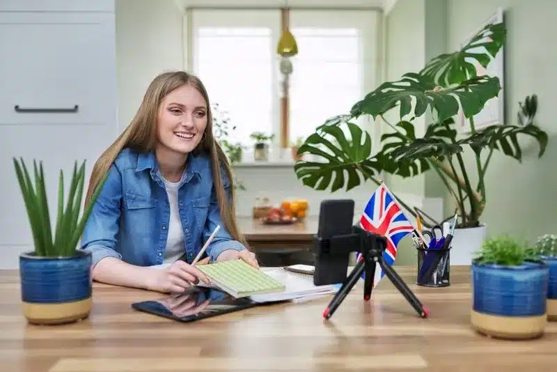 Mosolygó diák jegyzetel növények és brit zászló mellett, a Café English garantált eredményű, anyanyelvi beszédóráján.