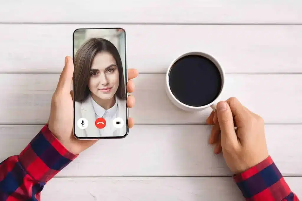 A Chat Mate online angol társalgáshoz illően kézben tartott telefonon mosolygó nő látszik, mellette kávéval.