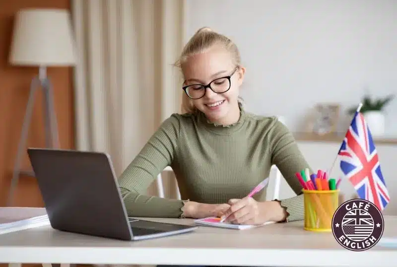 A mosolygó diák laptop és brit zászló mellett jegyzetel, miközben online angol tanfolyamra készül anyanyelvi tanárral.