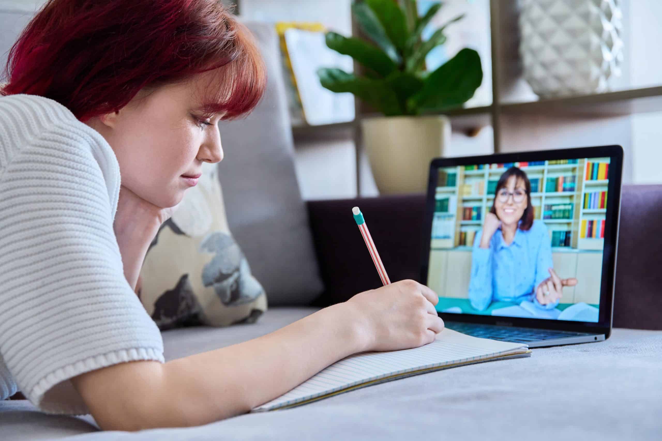 Egy tanuló jegyzetel, miközben laptopján tanára mutatja, hogyan segíthet az online tanfolyam a beszéd tanulásban.
