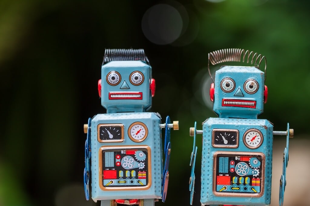 Két kék játékrobot áll zöld háttér előtt, az AI Chatbotok Forradalma az Angol Nyelvtanulásban című elemzést idézve.