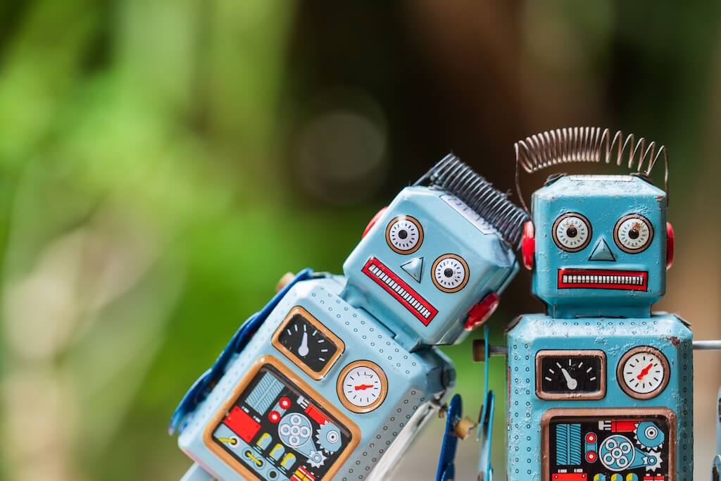 Két kék robot áll zöld, elmosott háttér előtt az AI Chatbotok Forradalma az Angol Nyelvtanulásban, elemzés cikkhez